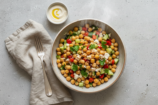 Chickpea salad with vegetables in a bowl on a gray surface with a napkin and fork.